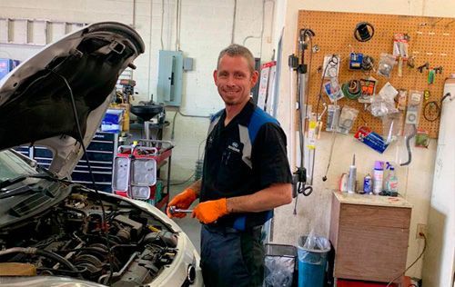 A man is working on a car in a garage with the hood open.