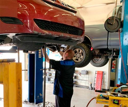 A man is working on a red car on a lift in a garage.