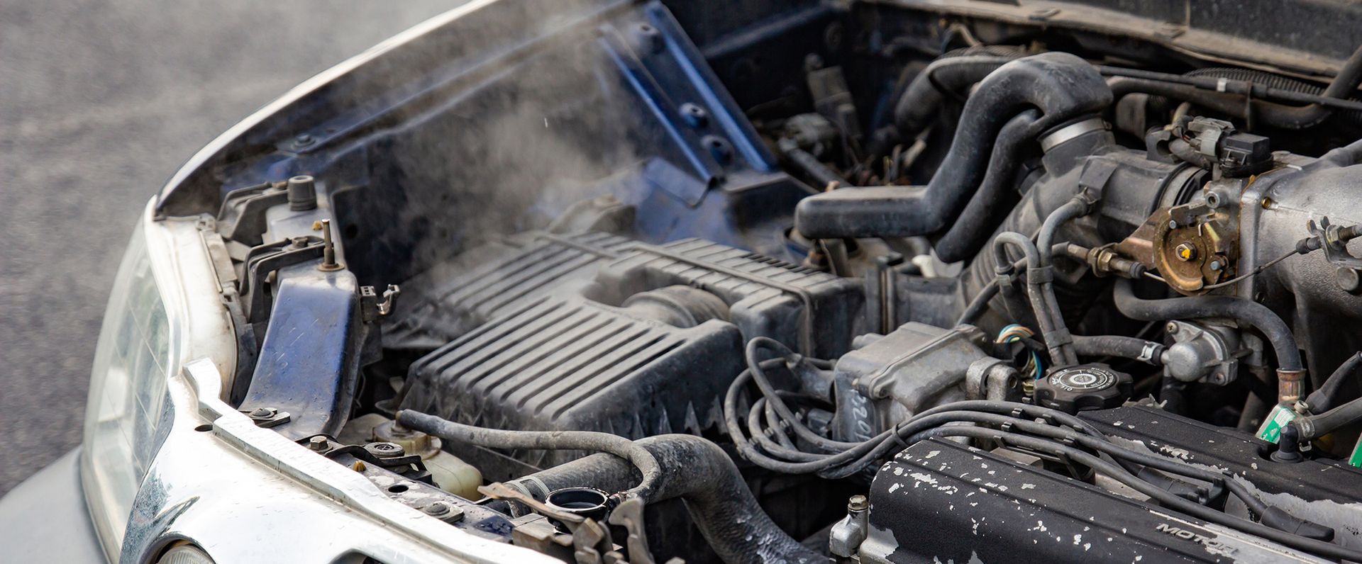 Damaged car engine bay with hood open and smoke rising after a fire