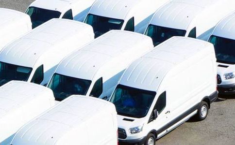 A row of white vans are parked in a parking lot.