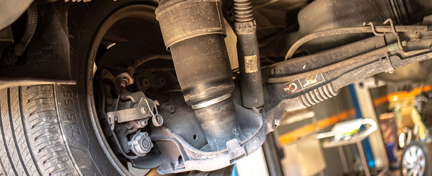 Undercarriage of a vehicle with exhaust and suspension components visible in a garage