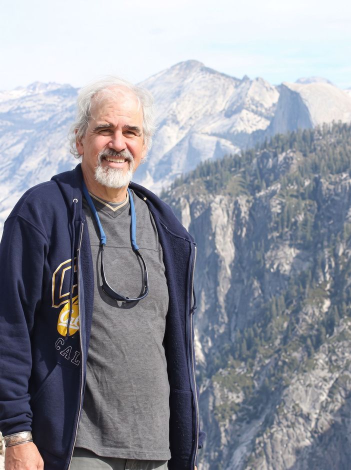 Man smiling outdoors in a navy jacket, with snowy mountains and cliffs in the background