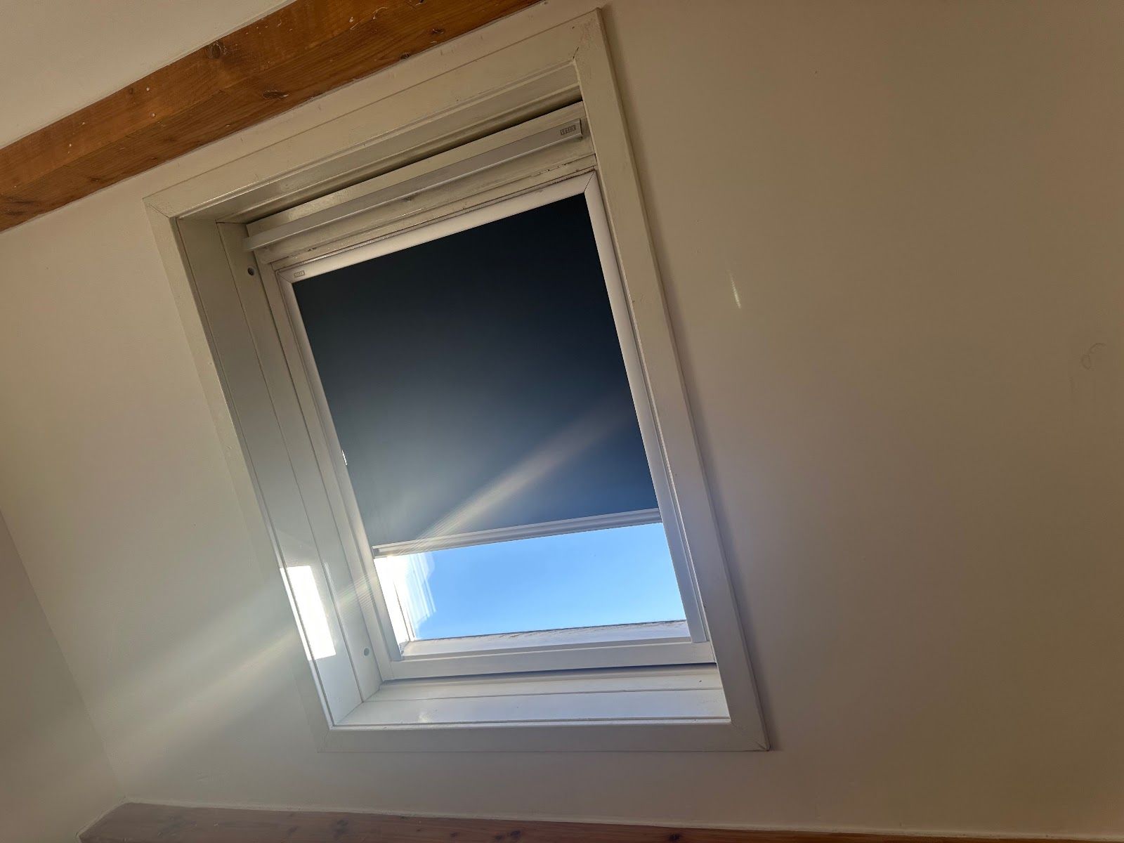 Tilted white window with partially closed dark blind and bright blue sky outside