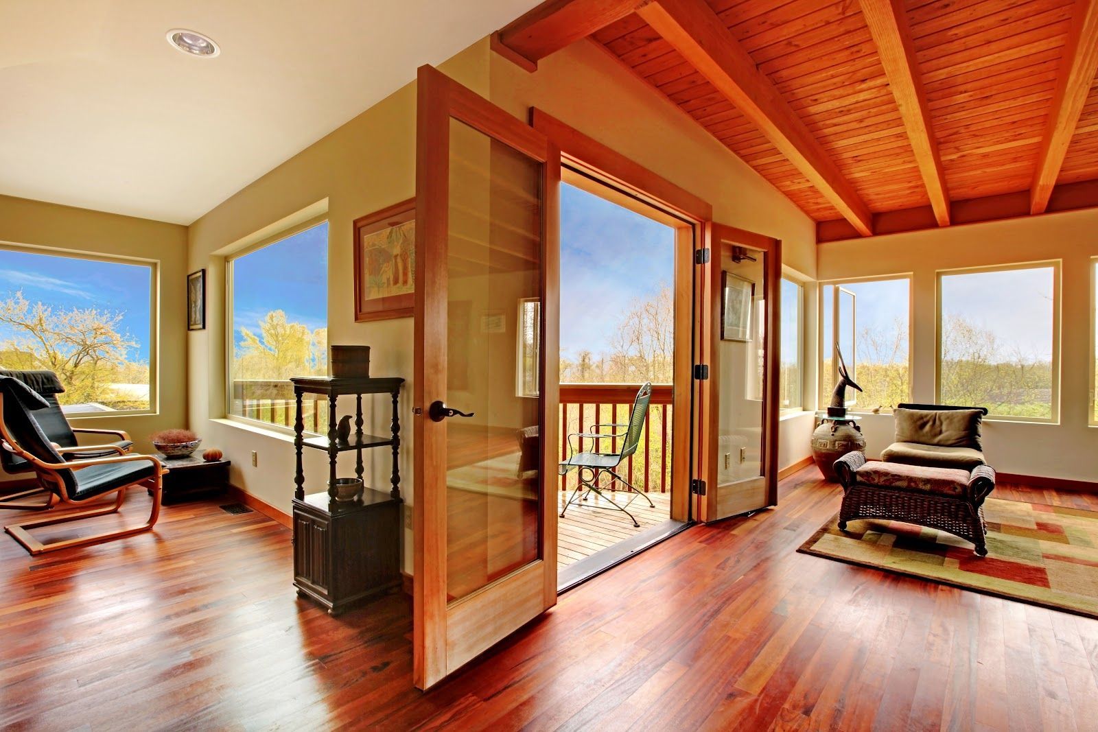 Bright open living room with wood floors, exposed ceiling beams, large windows, and balcony doors