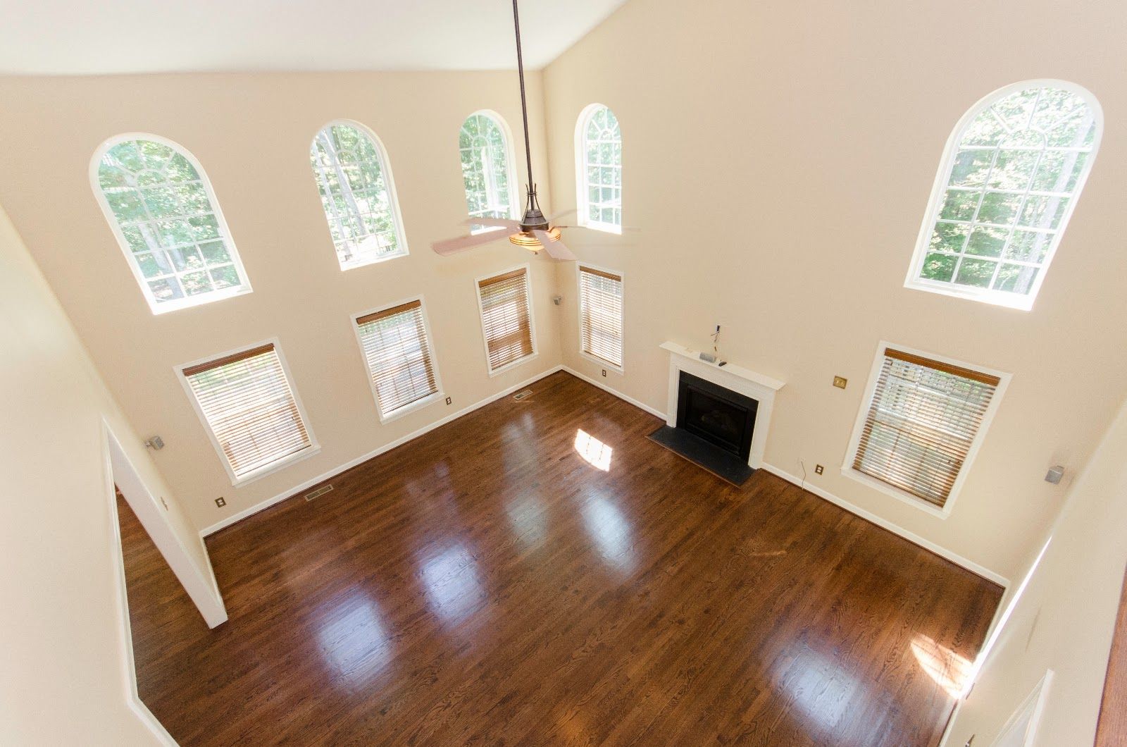 Spacious empty living room with hardwood floors, tall arched windows, and a fireplace.