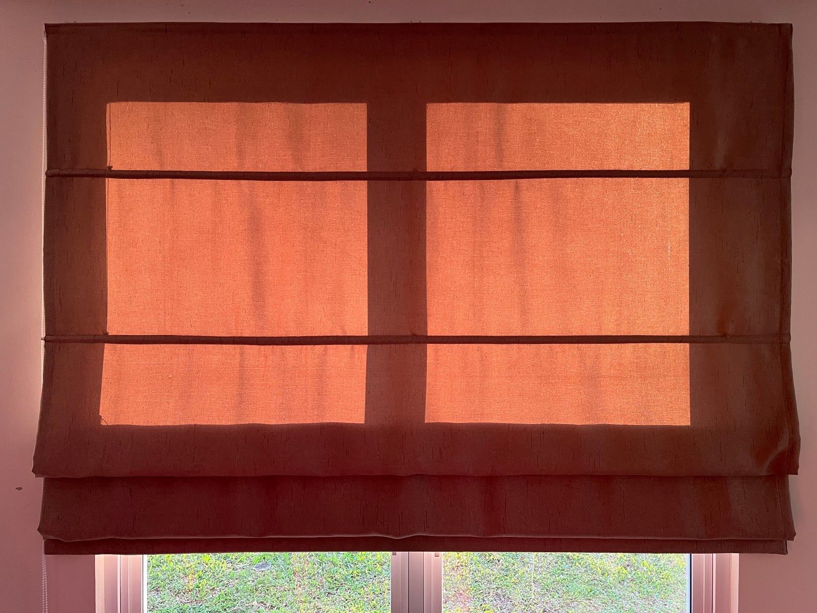 Closed brown window blinds with warm sunlight shining through slats