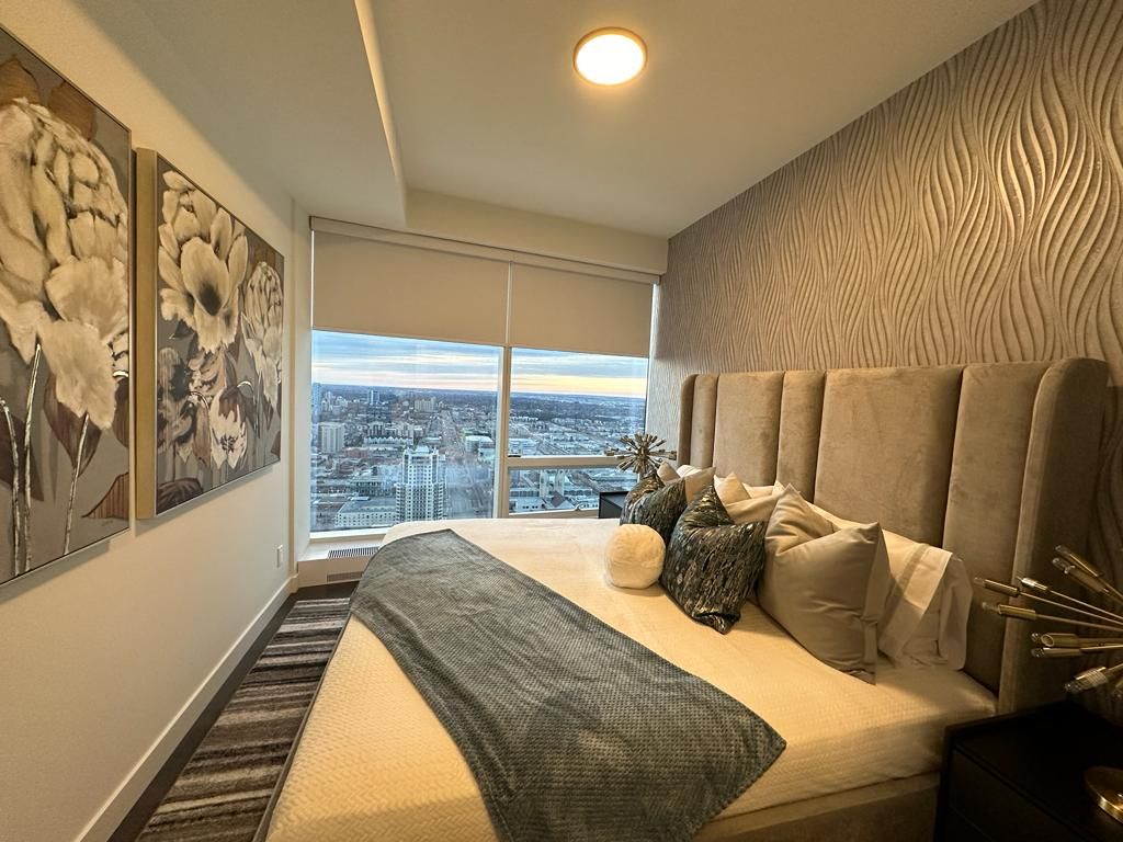 A bedroom with a large bed and a large window with a view of the city.