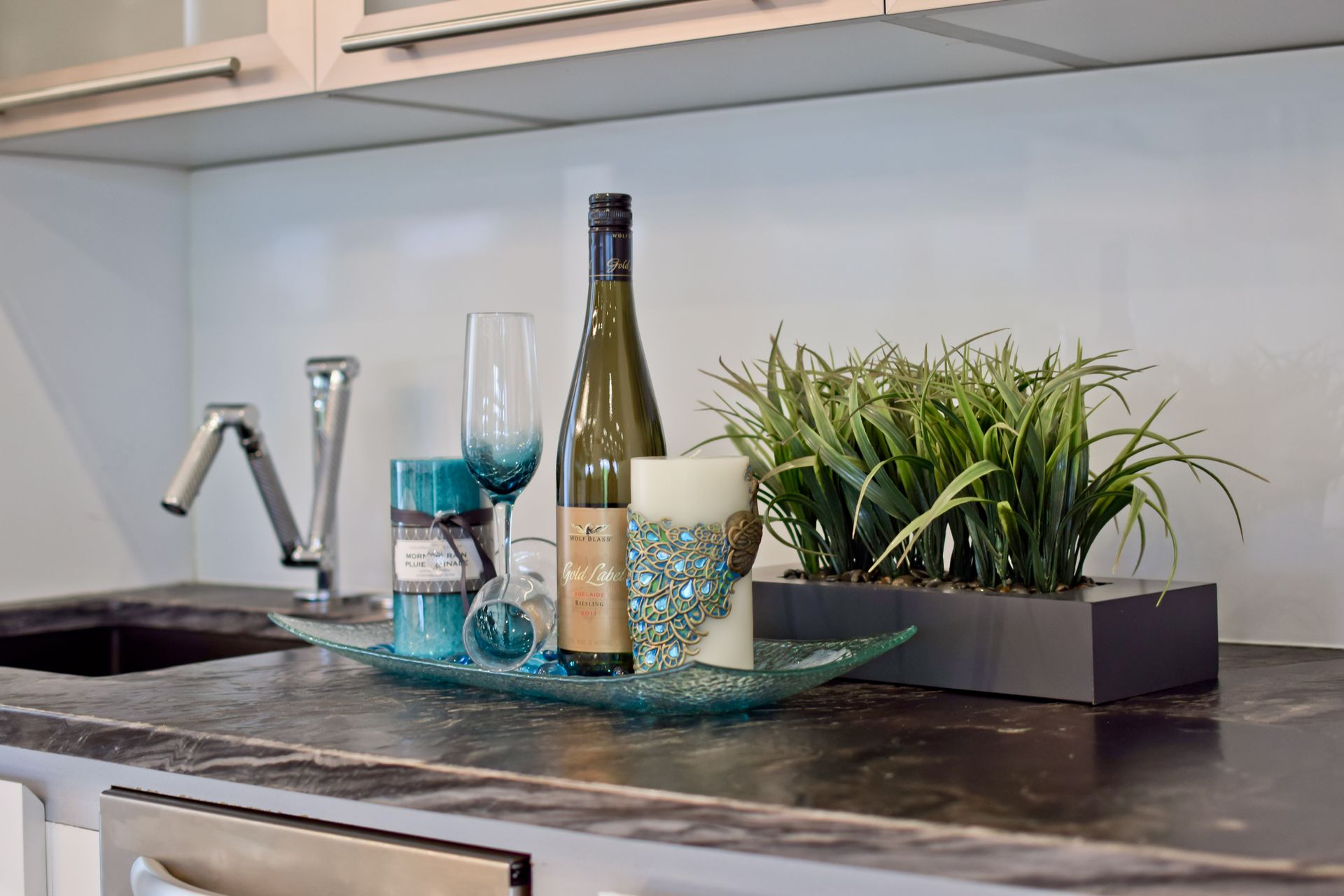 A kitchen counter with a bottle of wine , glasses , candles and plants.