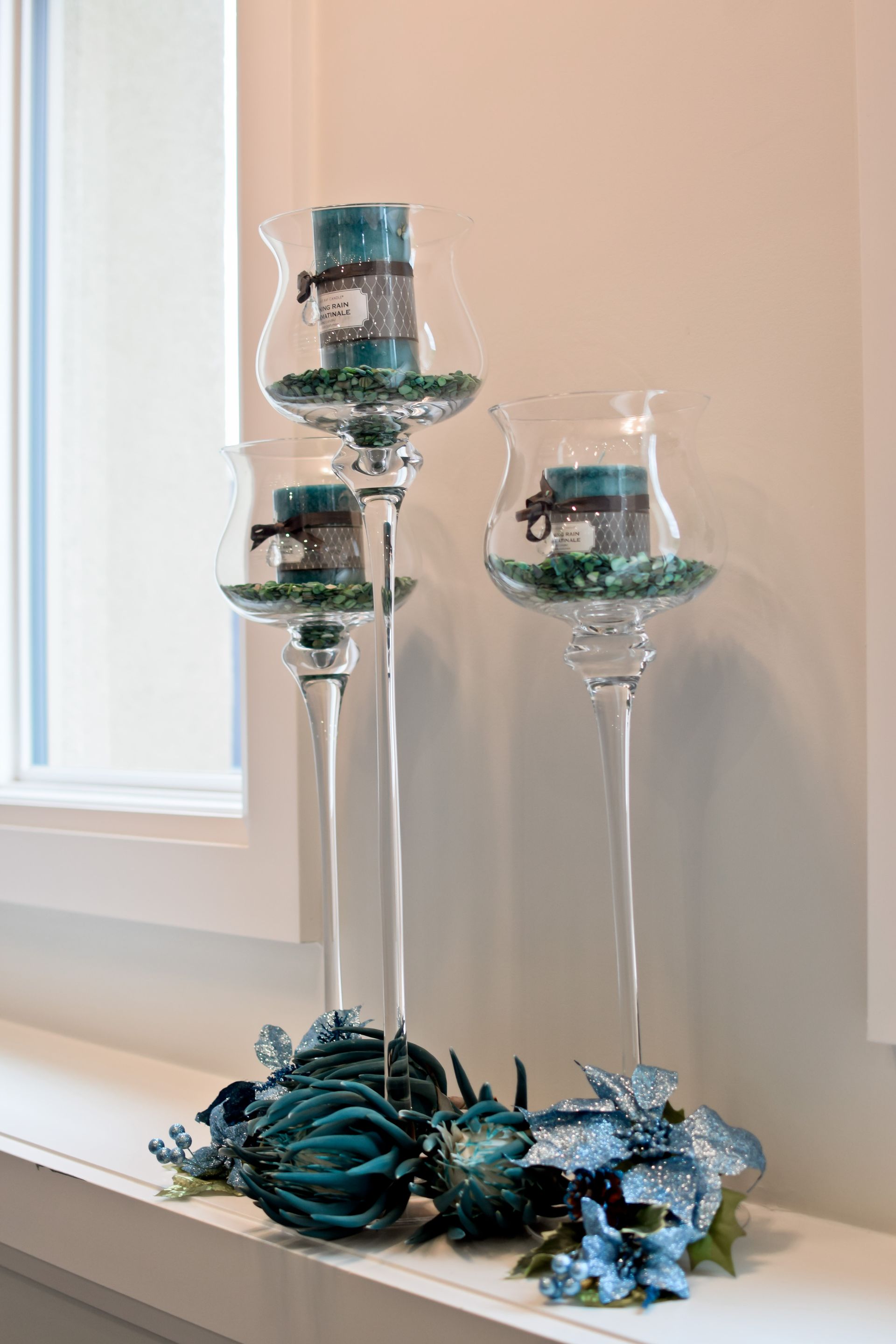 Three candle holders with candles in them are sitting on a window sill.