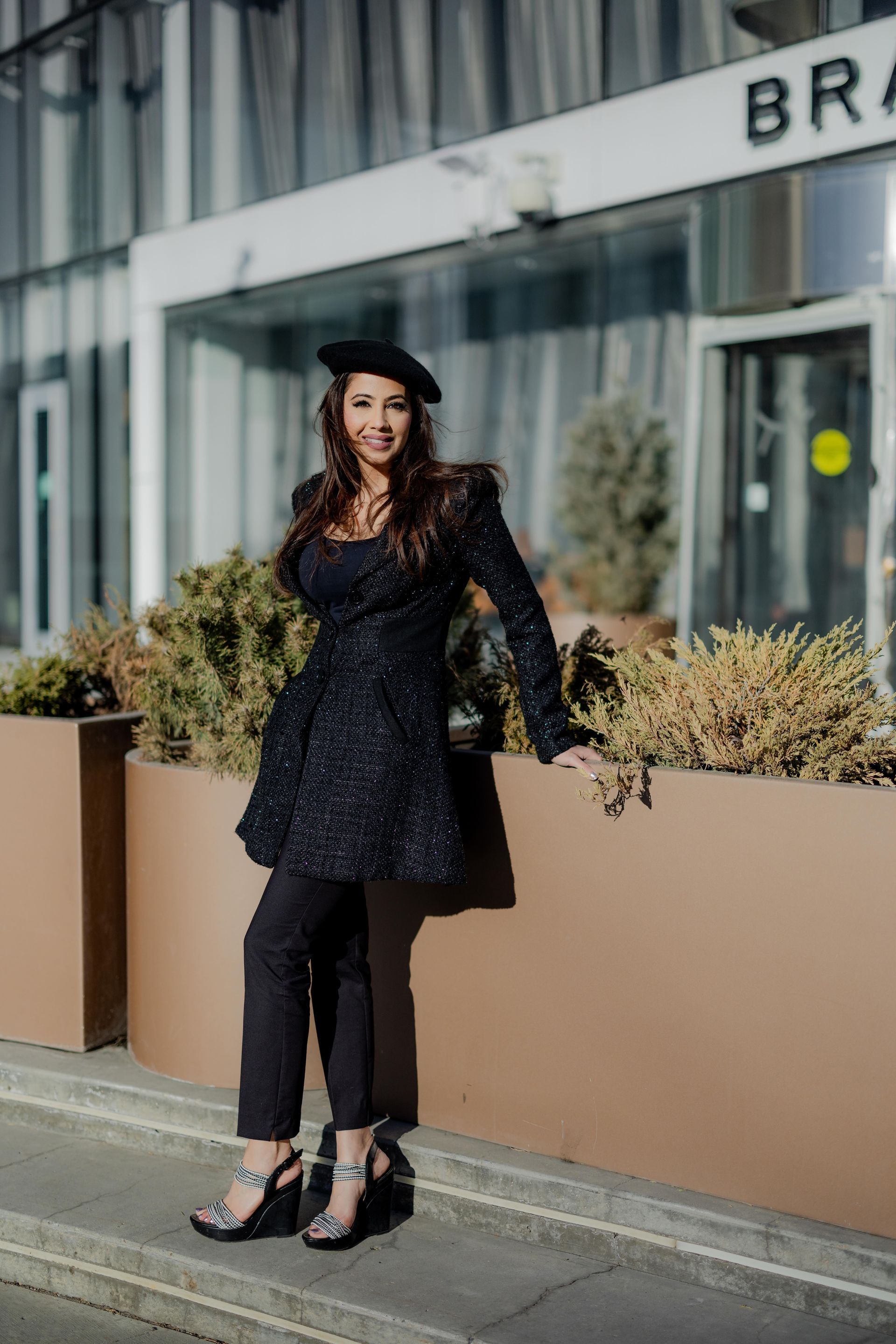 A woman in a black dress and beret is standing in front of a building.