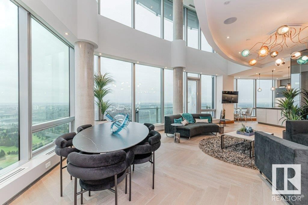 A living room with a dining table and chairs and a lot of windows.