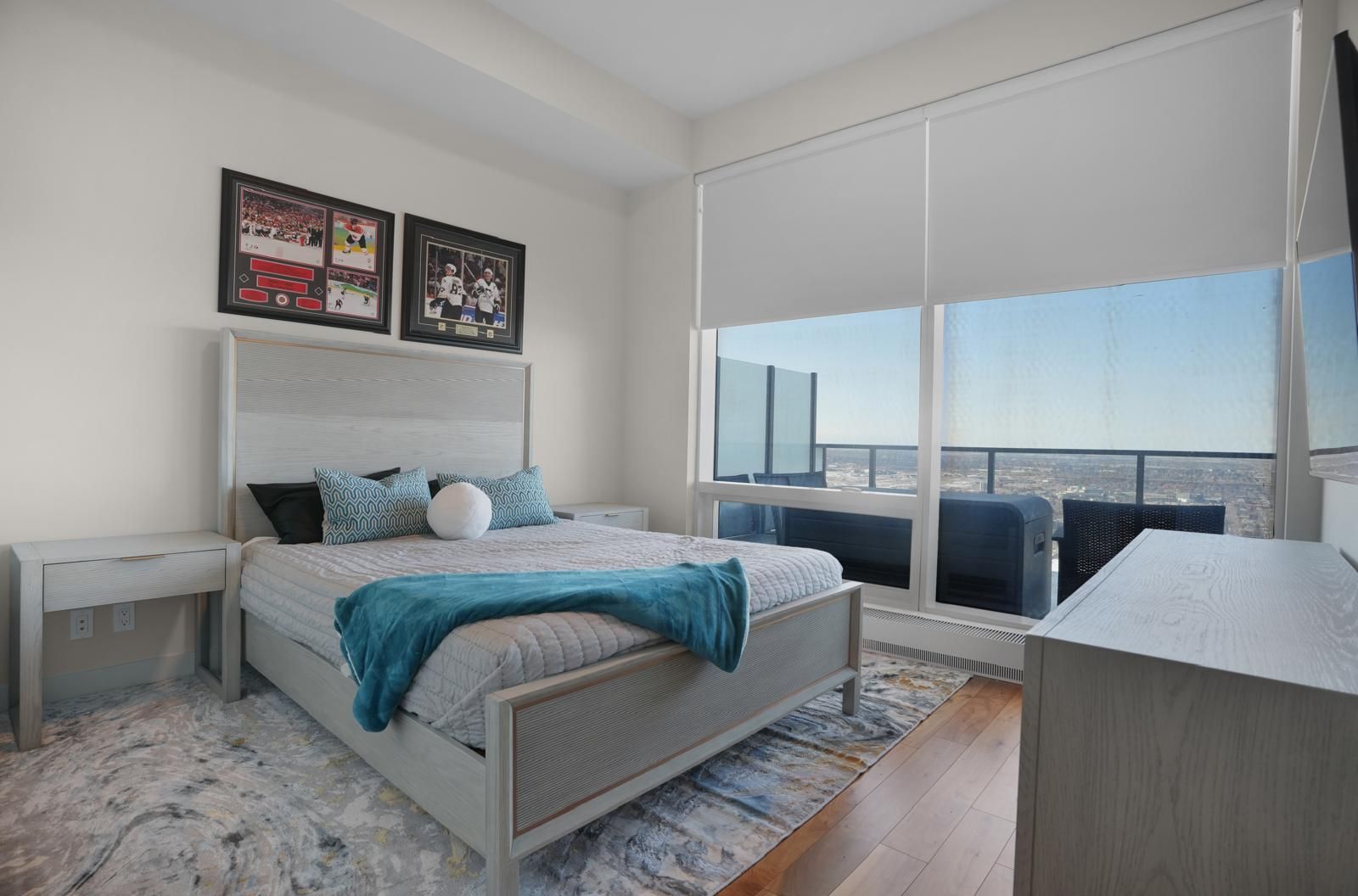 A bedroom with a king size bed , dresser , nightstand and large windows.