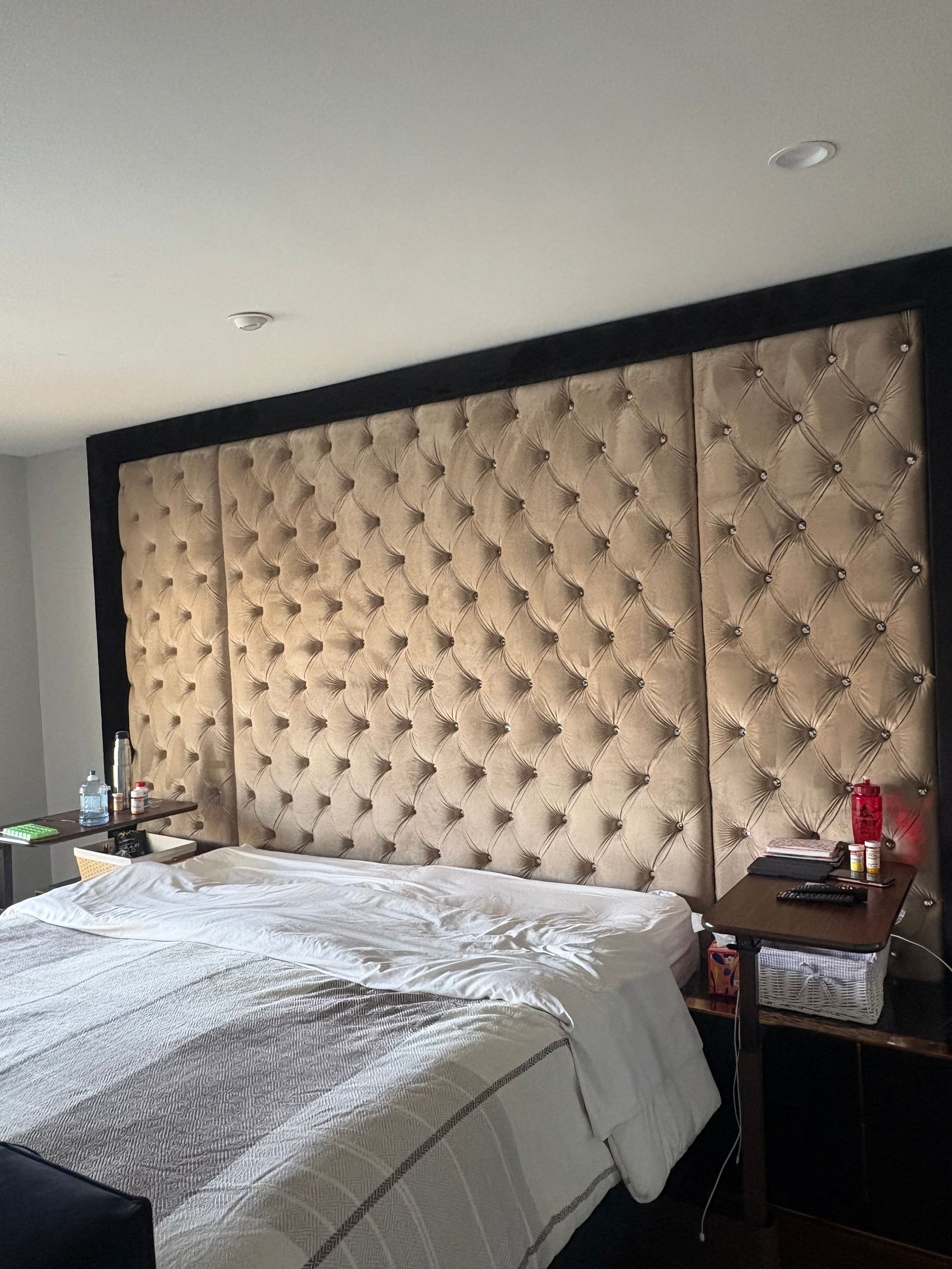 Large, tufted beige headboard above a bed with white and gray bedding. Dark brown trim frames the headboard.