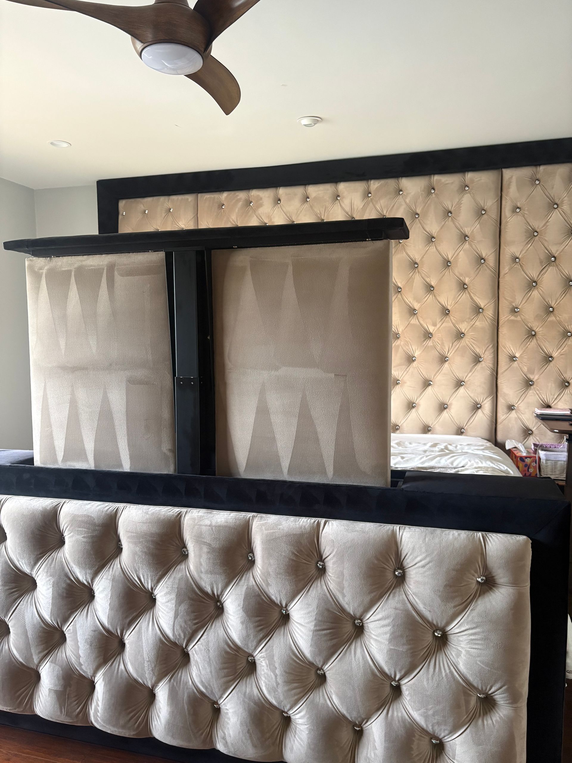 A tufted beige and black bed frame with a motorized TV lift in a bedroom.