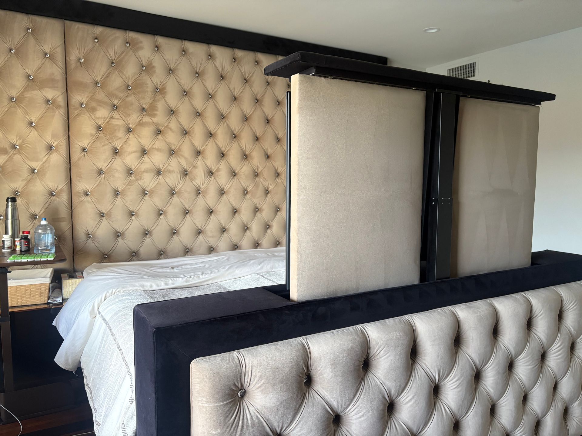 Tufted headboard with bed and a TV lift at the foot of the bed.