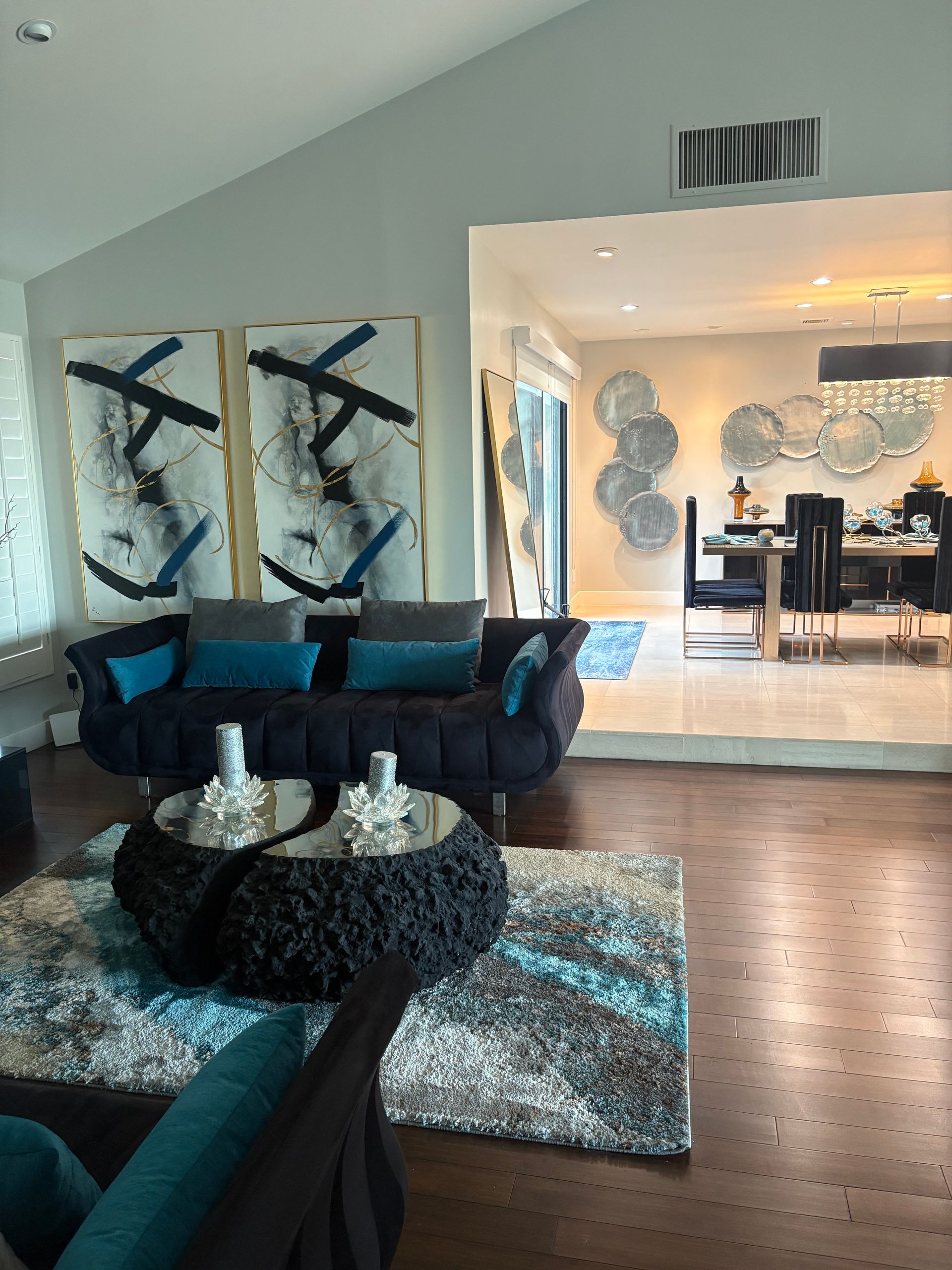 Living room with gray walls, dark sofa, blue accents, and abstract art; dining room visible in the background.