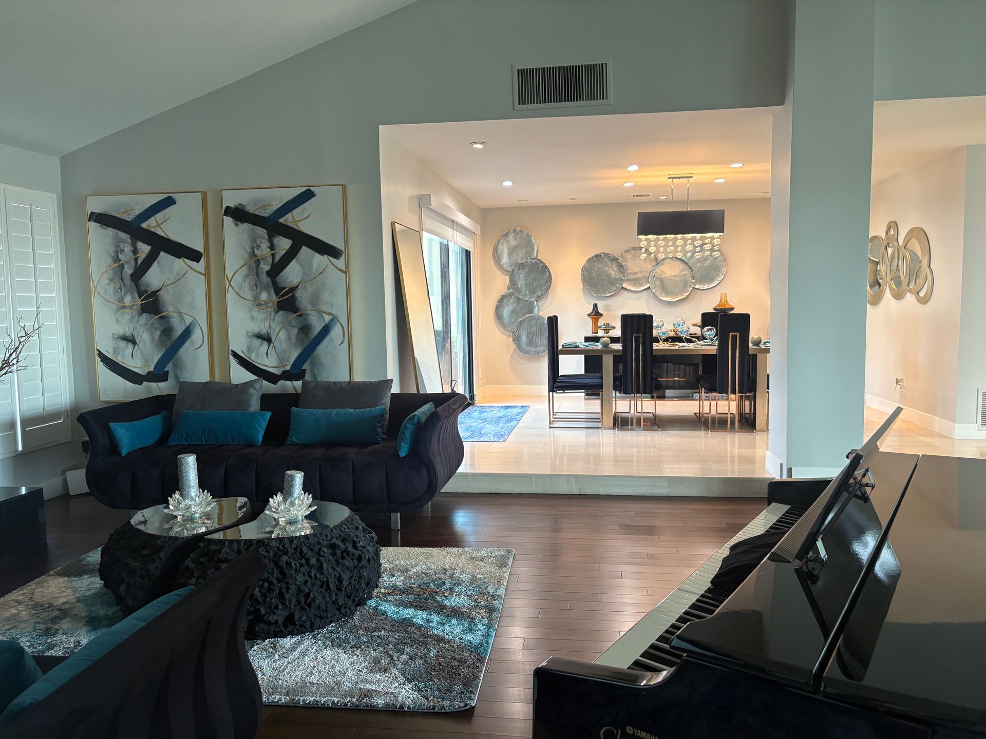 Living room with piano, sofa, abstract art, and view into dining room with table and chairs.