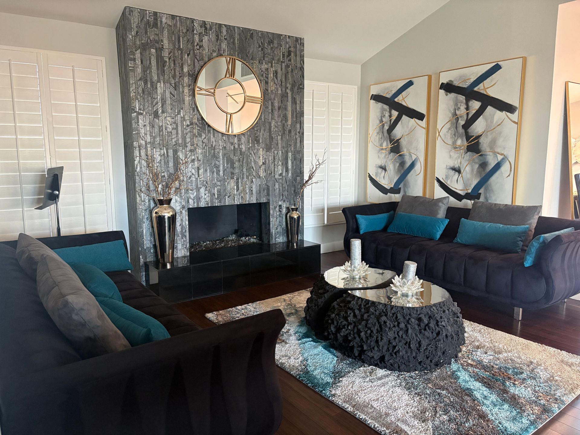 Living room with black furniture, teal pillows, a textured fireplace, and abstract art.