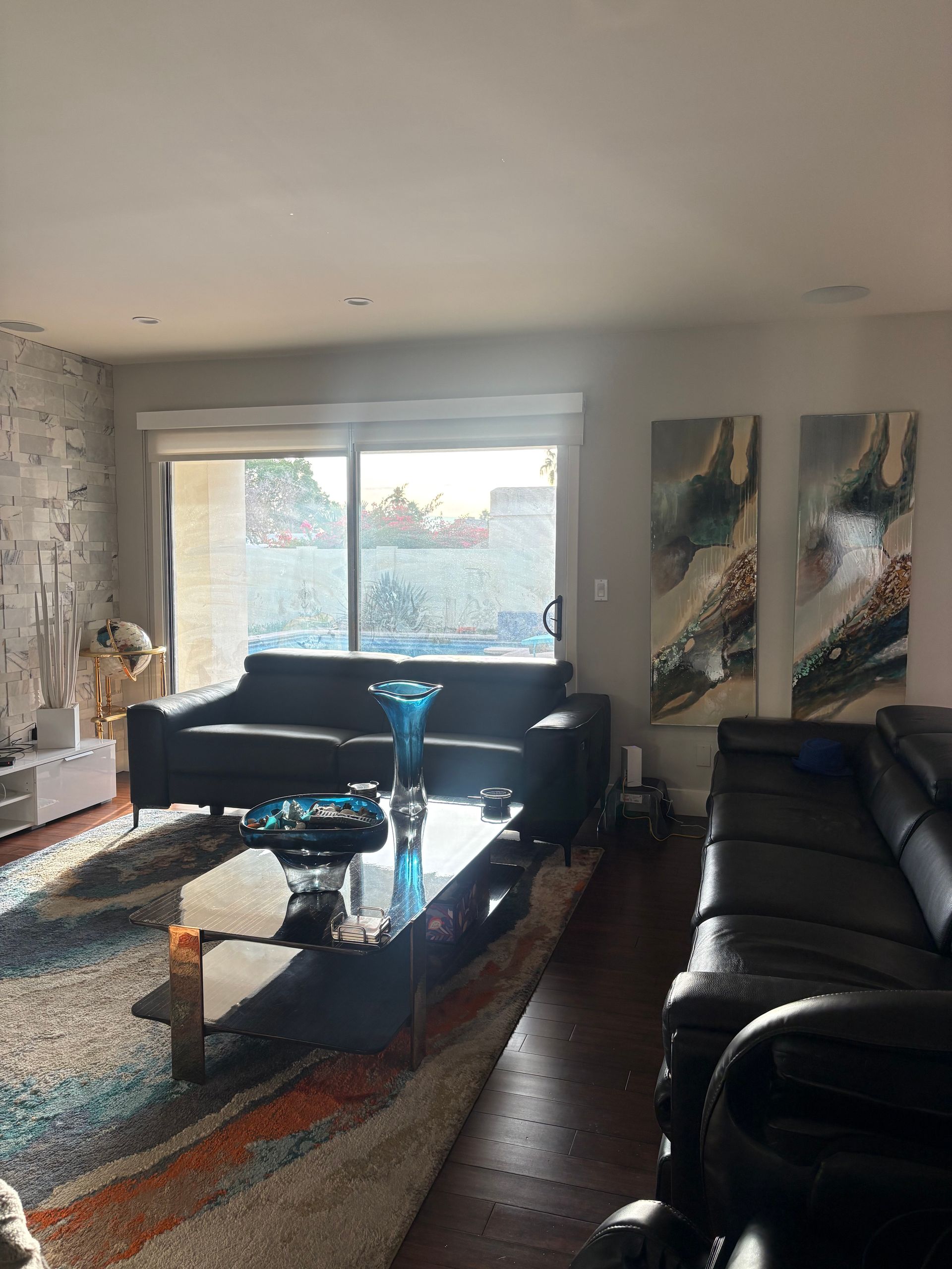 Living room with dark couches, glass coffee table, artwork, and large sliding glass door.