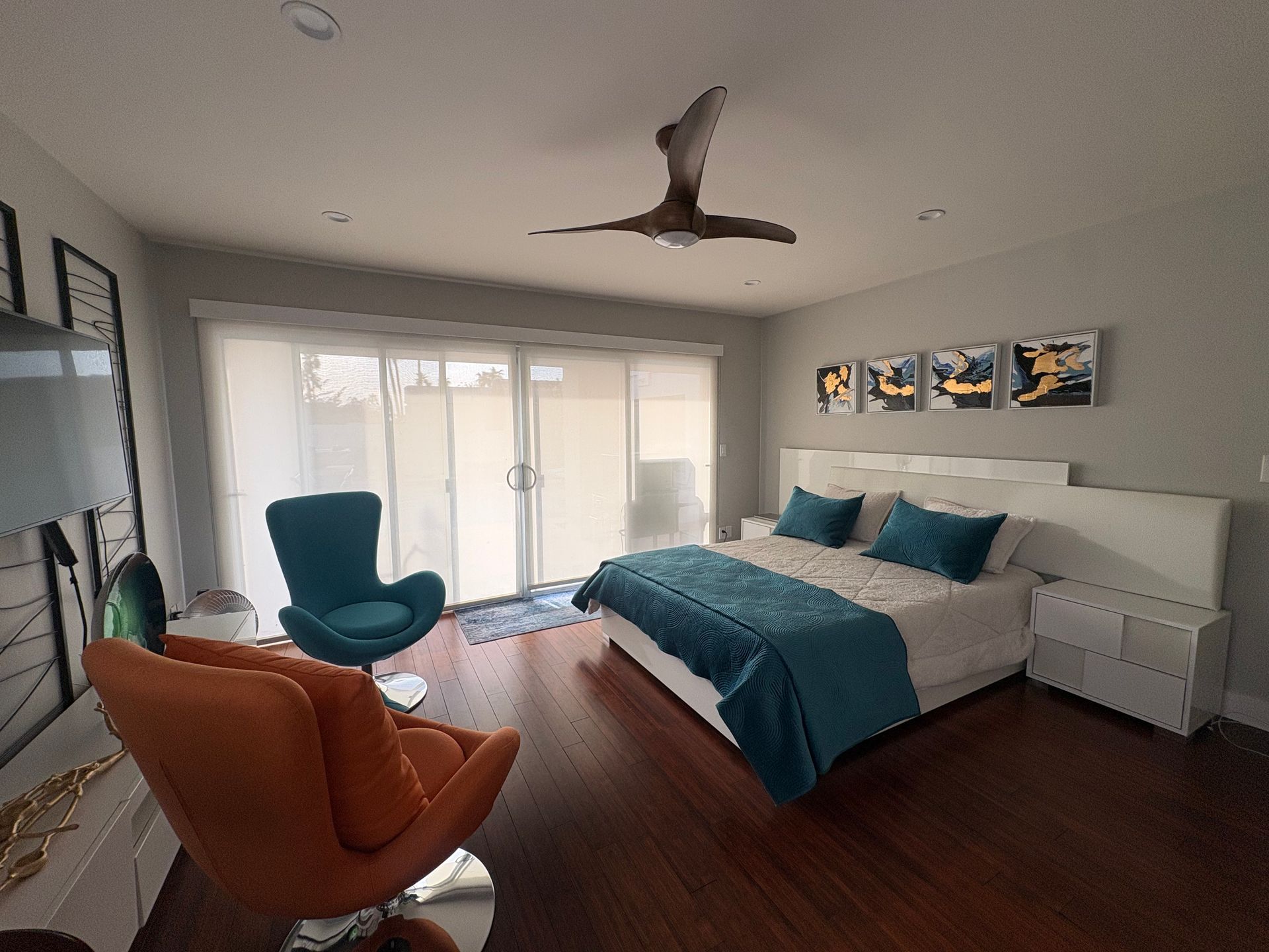Bedroom with bed, orange and teal chairs, sliding glass door, and art.