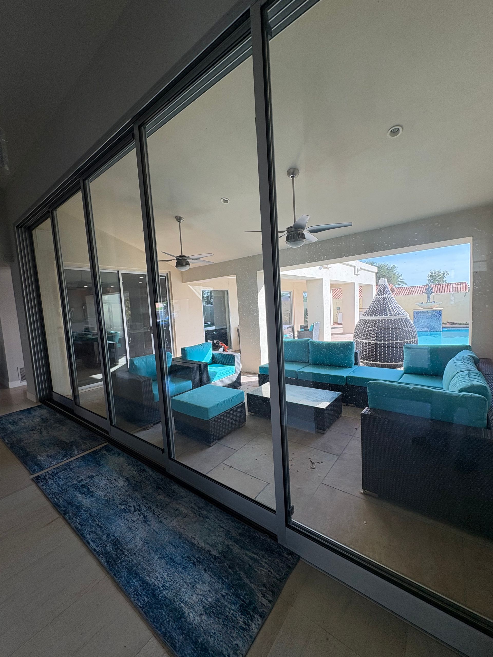 Sliding glass doors reflecting a patio with teal furniture, ceiling fans, and a view of the sky.