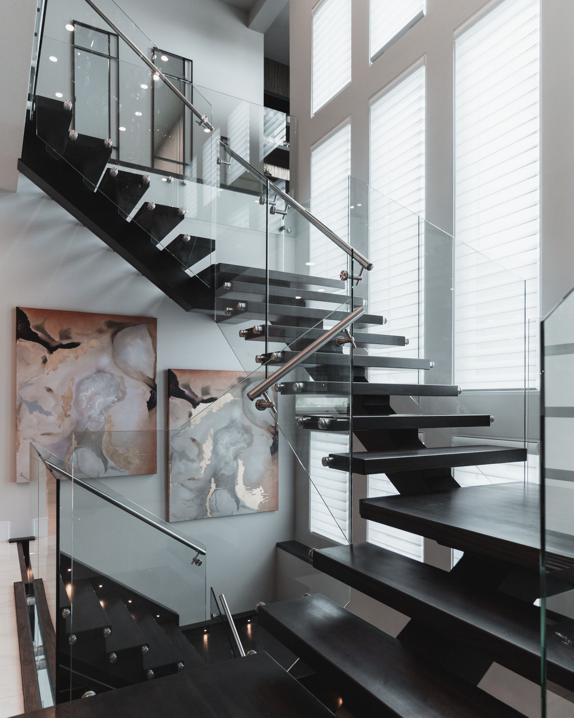 A staircase with a glass railing and a painting on the wall
