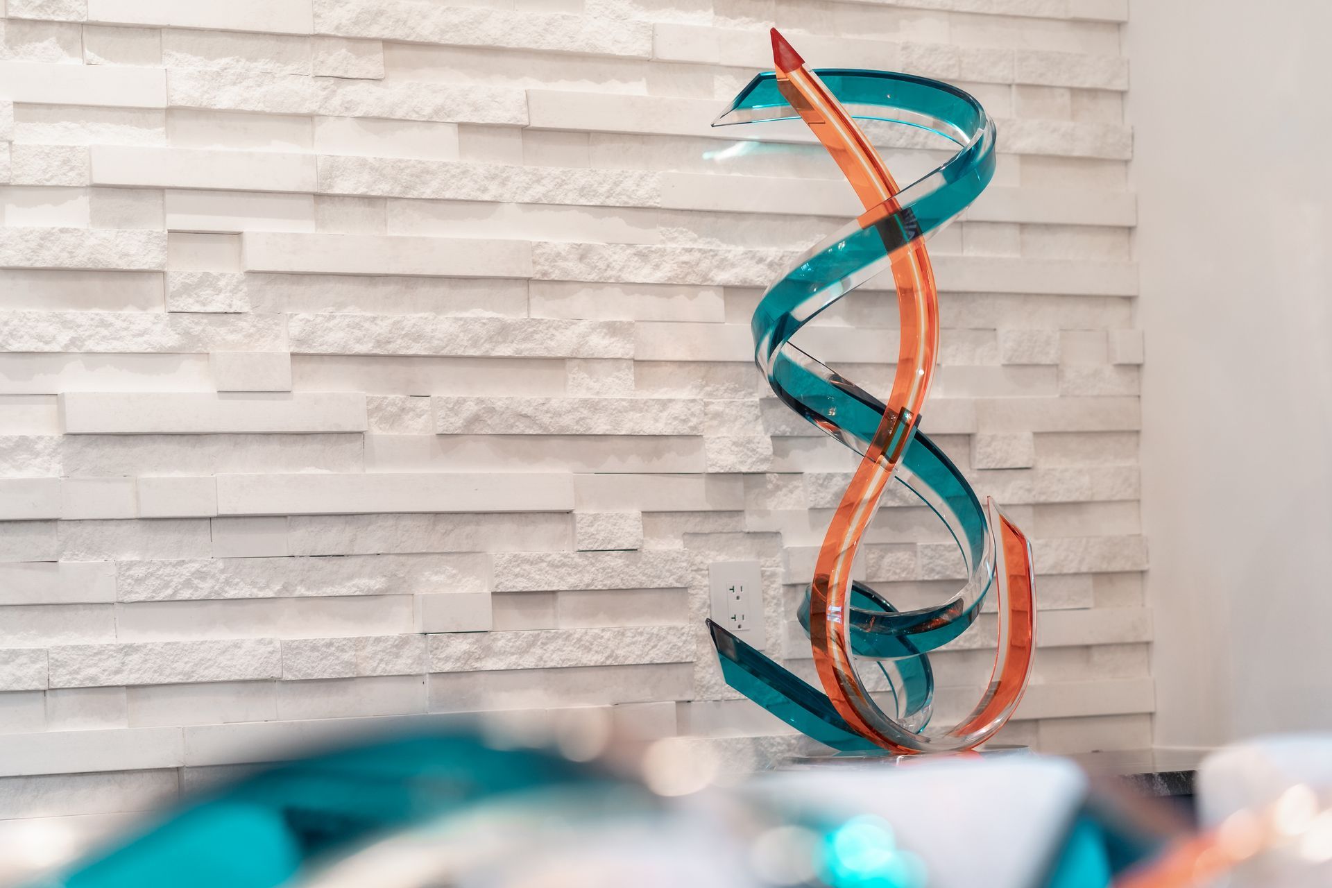 A blue and orange sculpture is sitting in front of a brick wall.