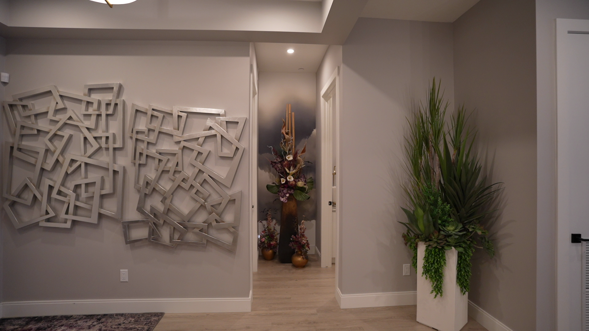 A hallway with a painting on the wall and a potted plant.