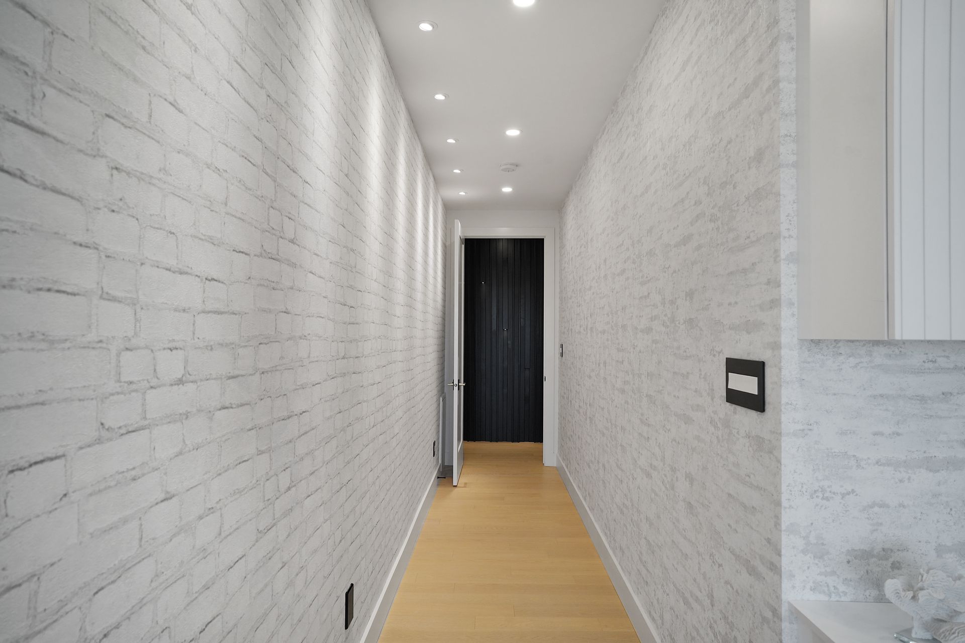 A long hallway with white brick walls and a wooden floor.
