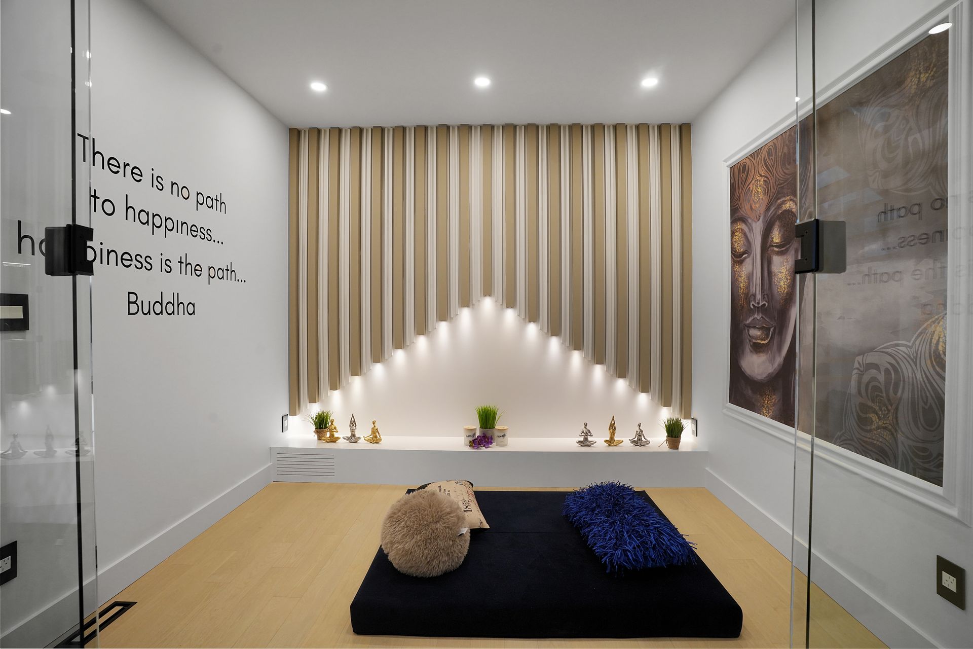 A meditation room with a black mat, cushions, and a Buddha artwork. Cream-colored curtains and a built-in shelf with candles and plants complete the tranquil setting.