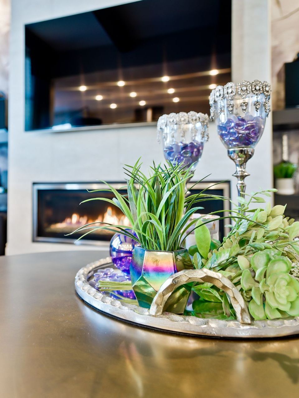A tray with flowers and candles on it is on a table in front of a fireplace.