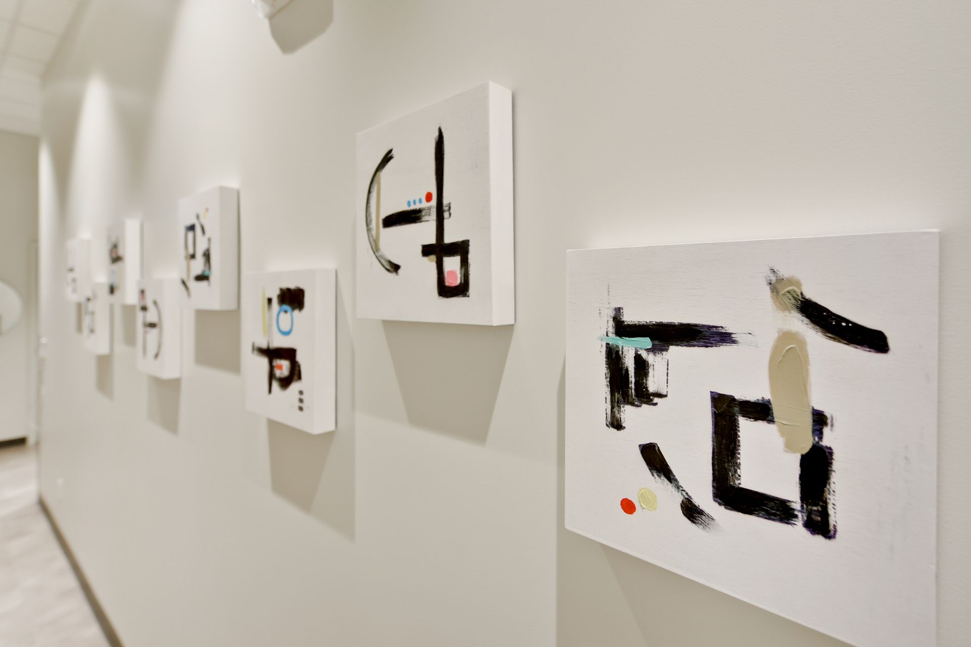 A row of paintings are hanging on a wall in a hallway.