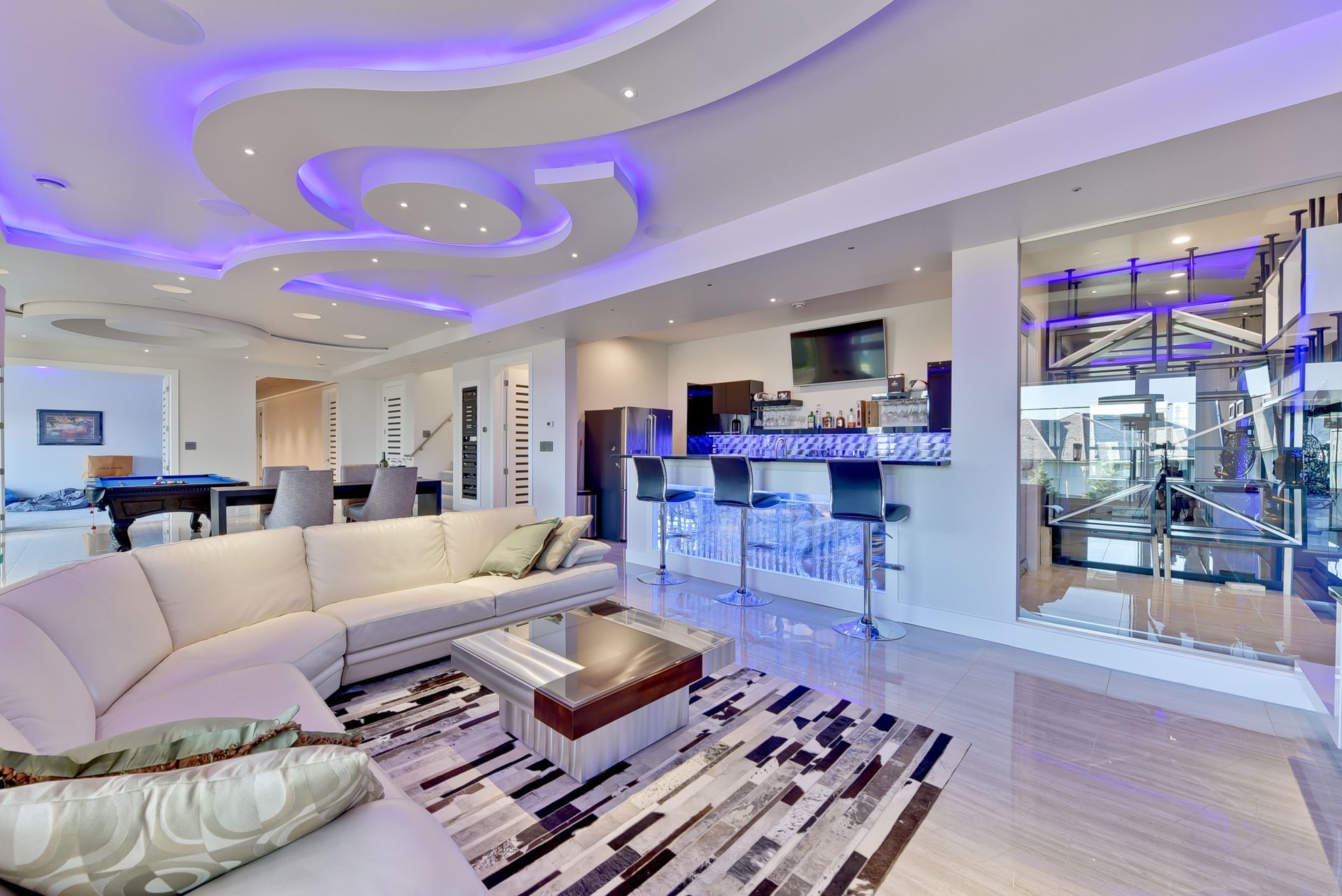 A living room with a couch , table , and purple lights on the ceiling.
