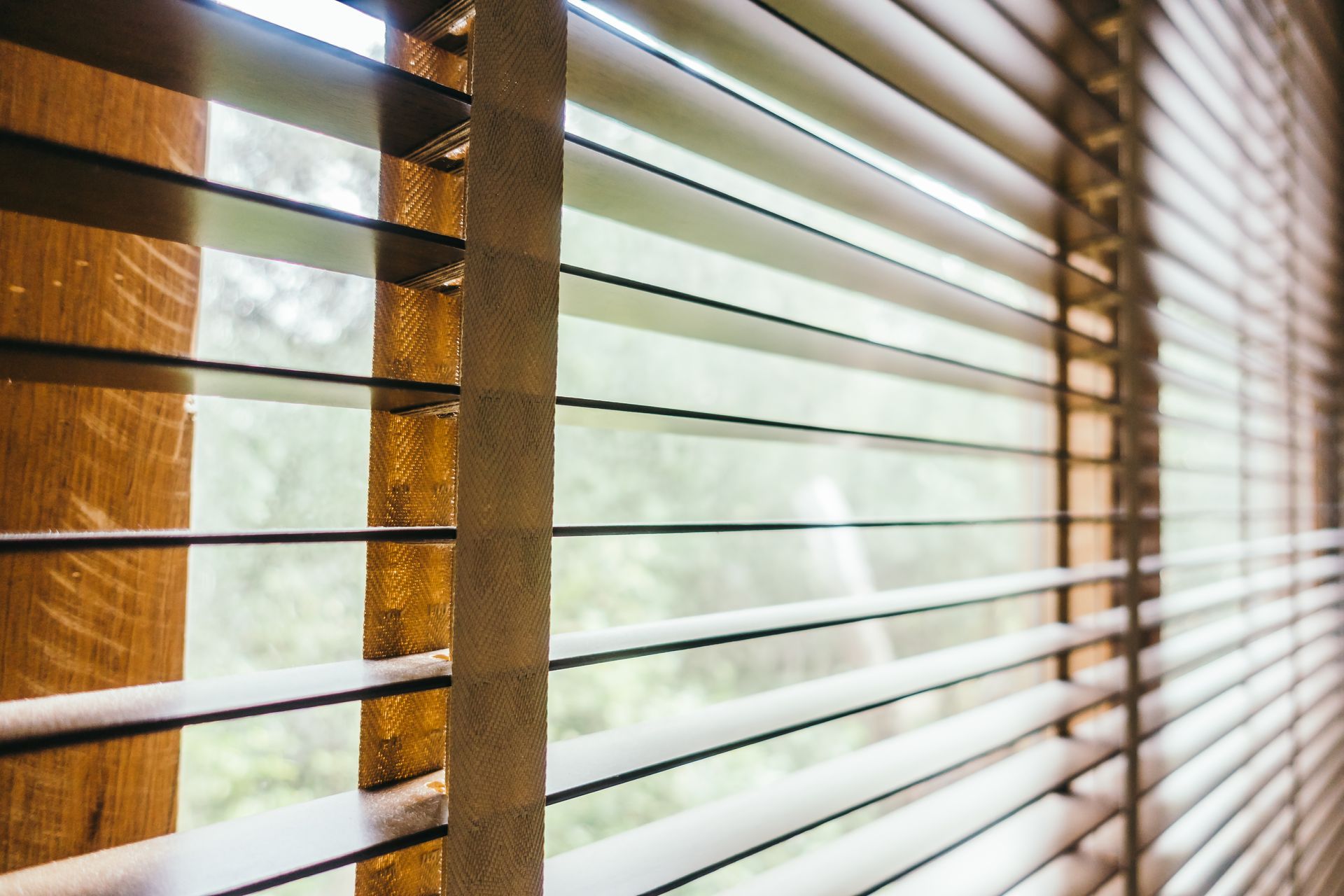 Wooden blinds, partially open, letting in light. Focus on the slats and surrounding window frame.
