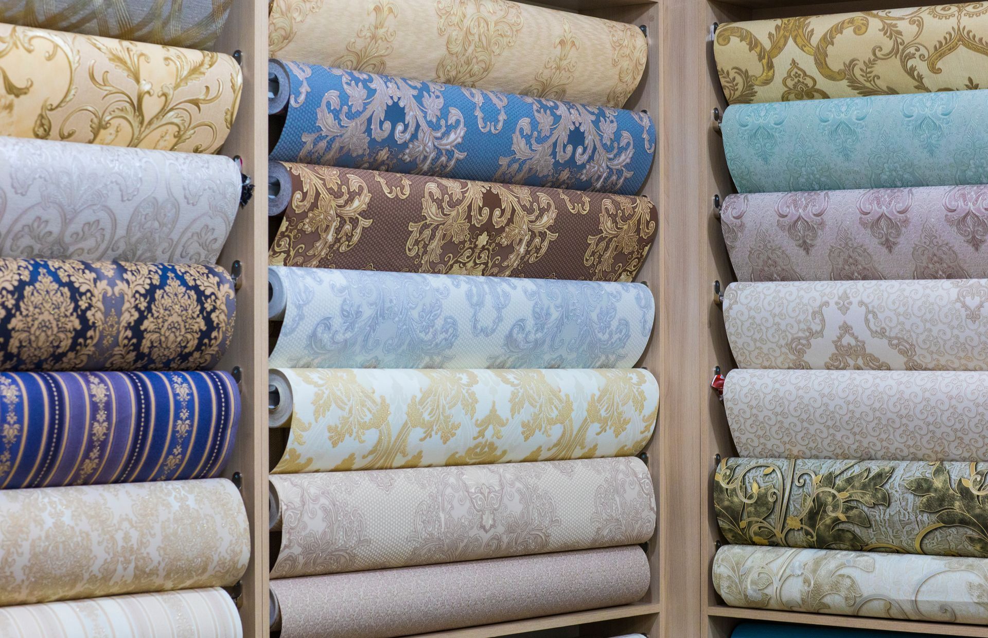 Shelves stacked with rolls of patterned wallpaper in cream, blue, and green tones