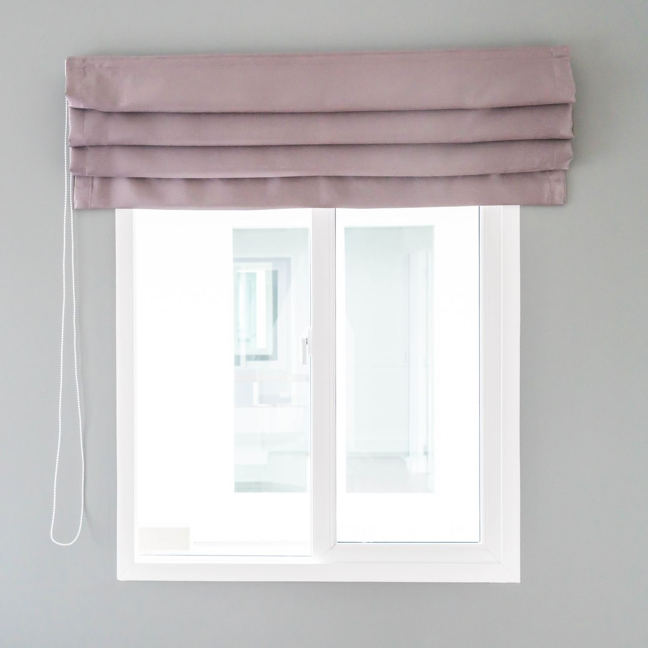 Window with mauve Roman shade, inside white frame. Gray wall.