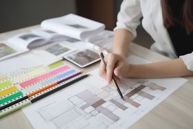 A woman is sitting at a table drawing a floor plan with a pencil.