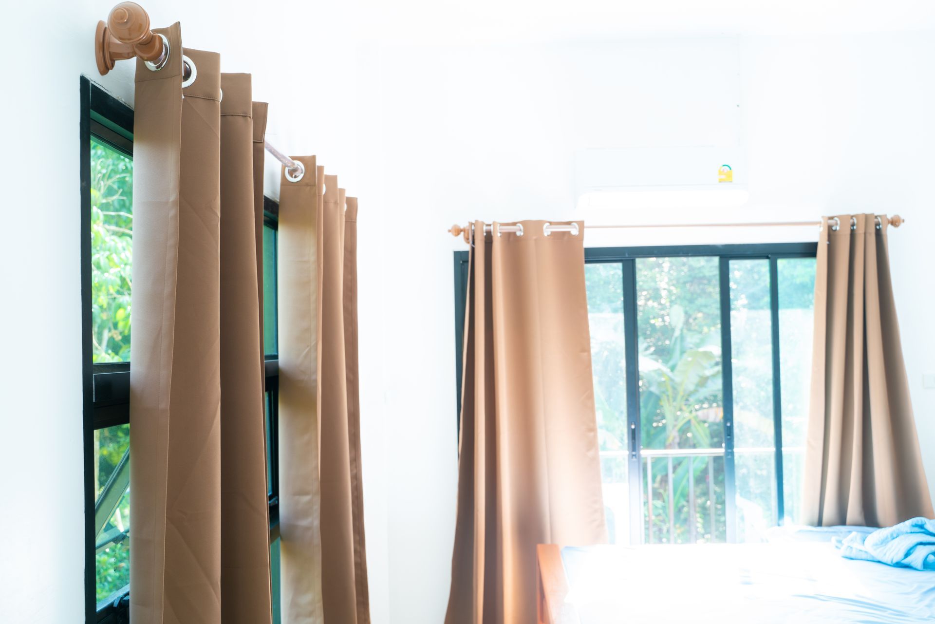 Brown curtains hanging in front of windows, white walls, sunny daylight.