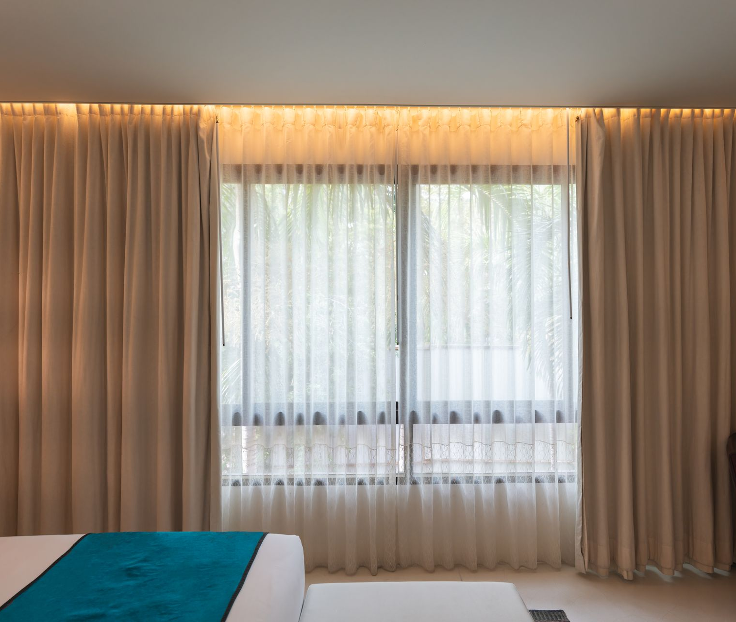 Beige curtains frame a window with a sheer white curtain. Warm lighting glows from above.