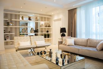 Modern living room with a beige sofa, two white chairs, a mirrored coffee table, and open shelving on a striped wall.
