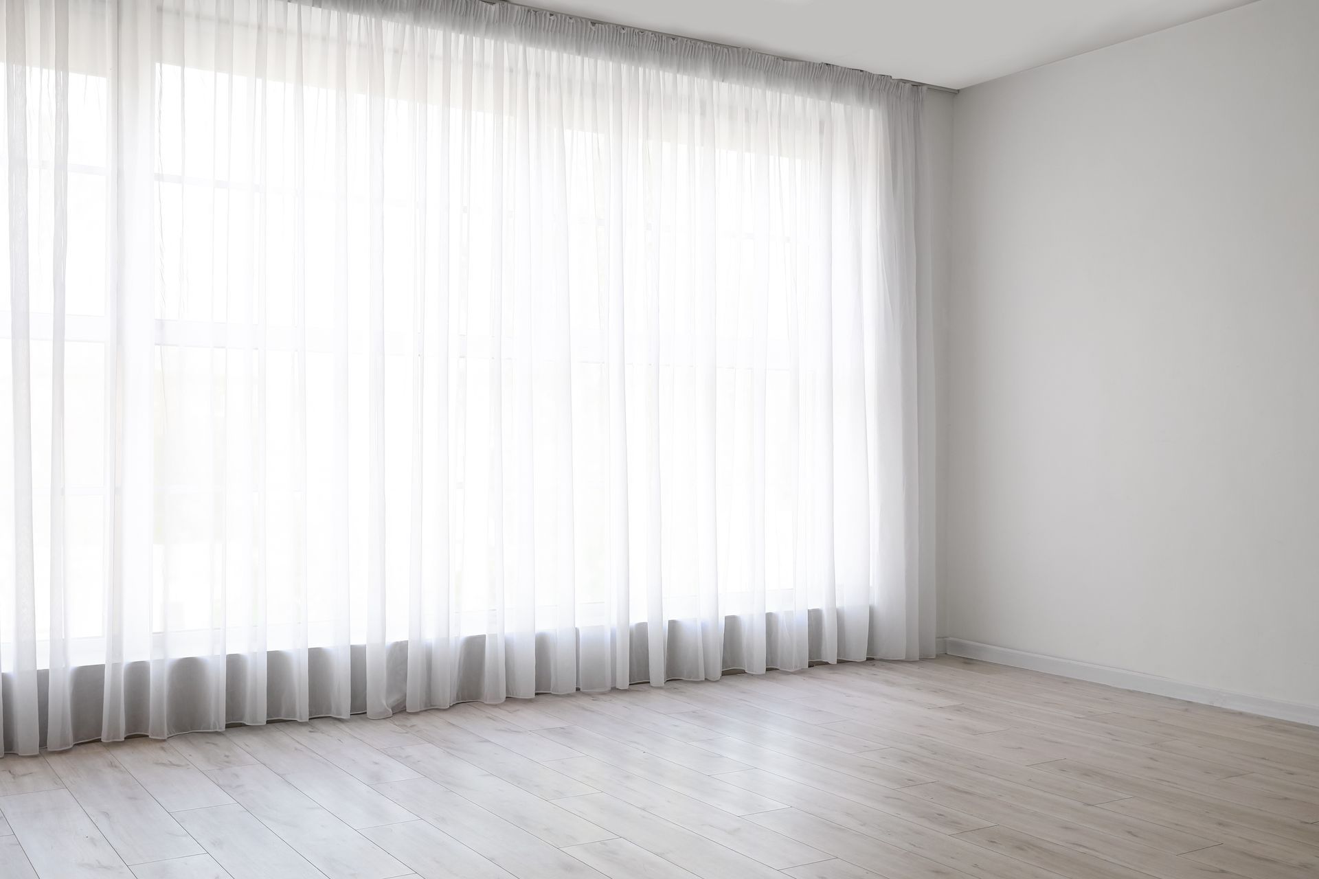 An empty room with a large window and white curtains.