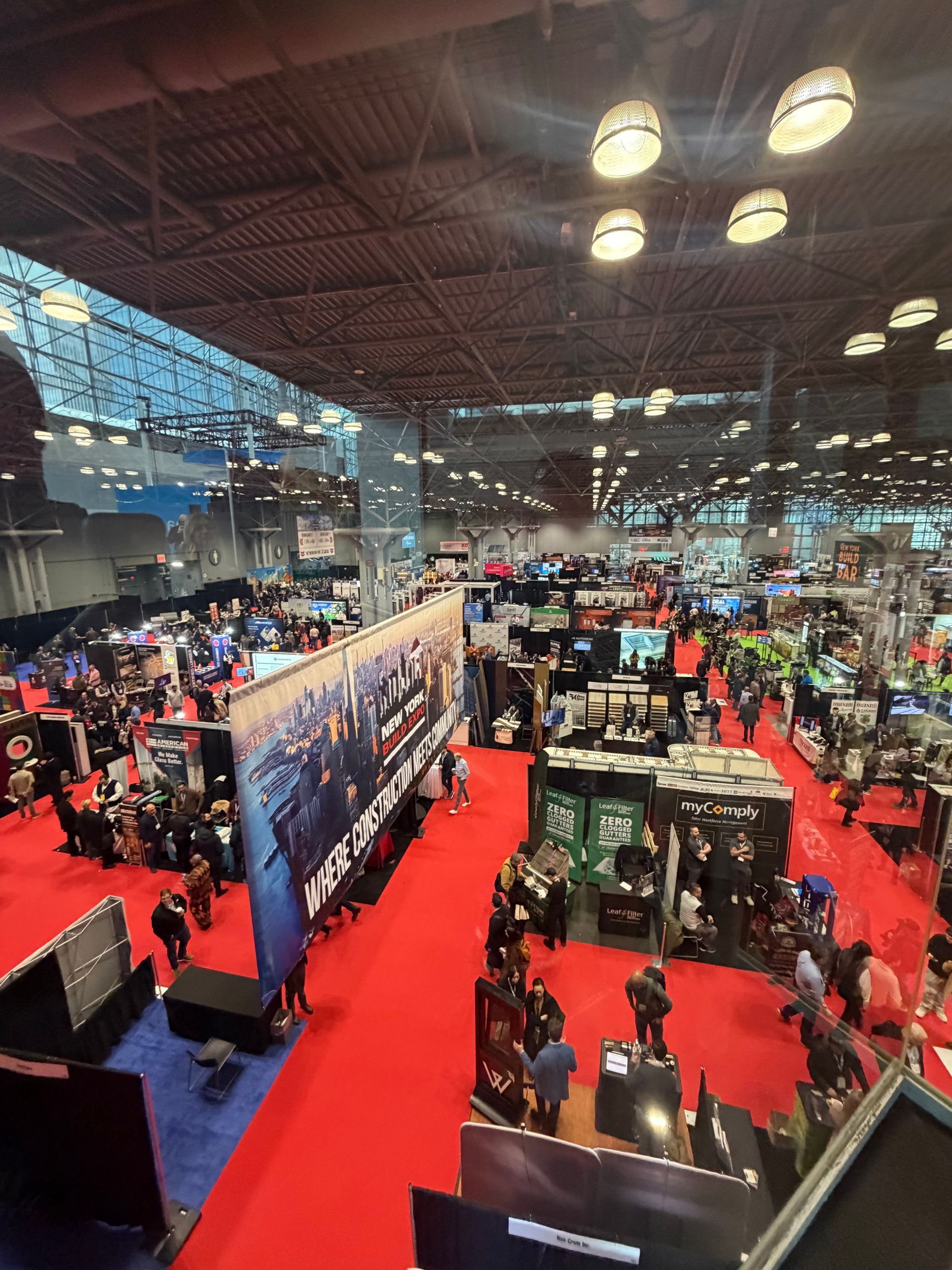 Crowded convention hall with red carpet aisles, booths, and many attendees under bright overhead lights