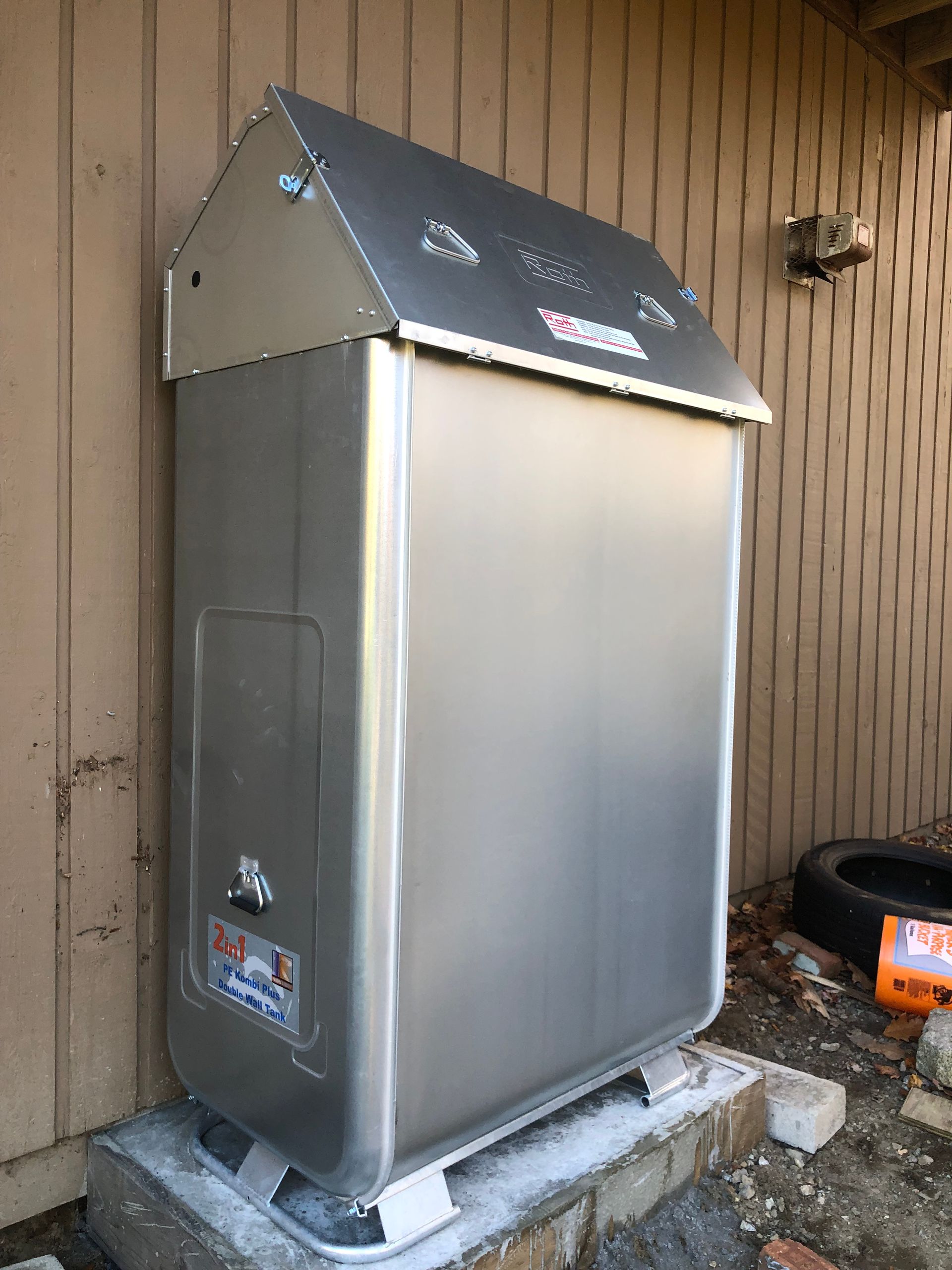 Outdoor stainless steel utility cabinet on a concrete pad beside a wood-paneled wall