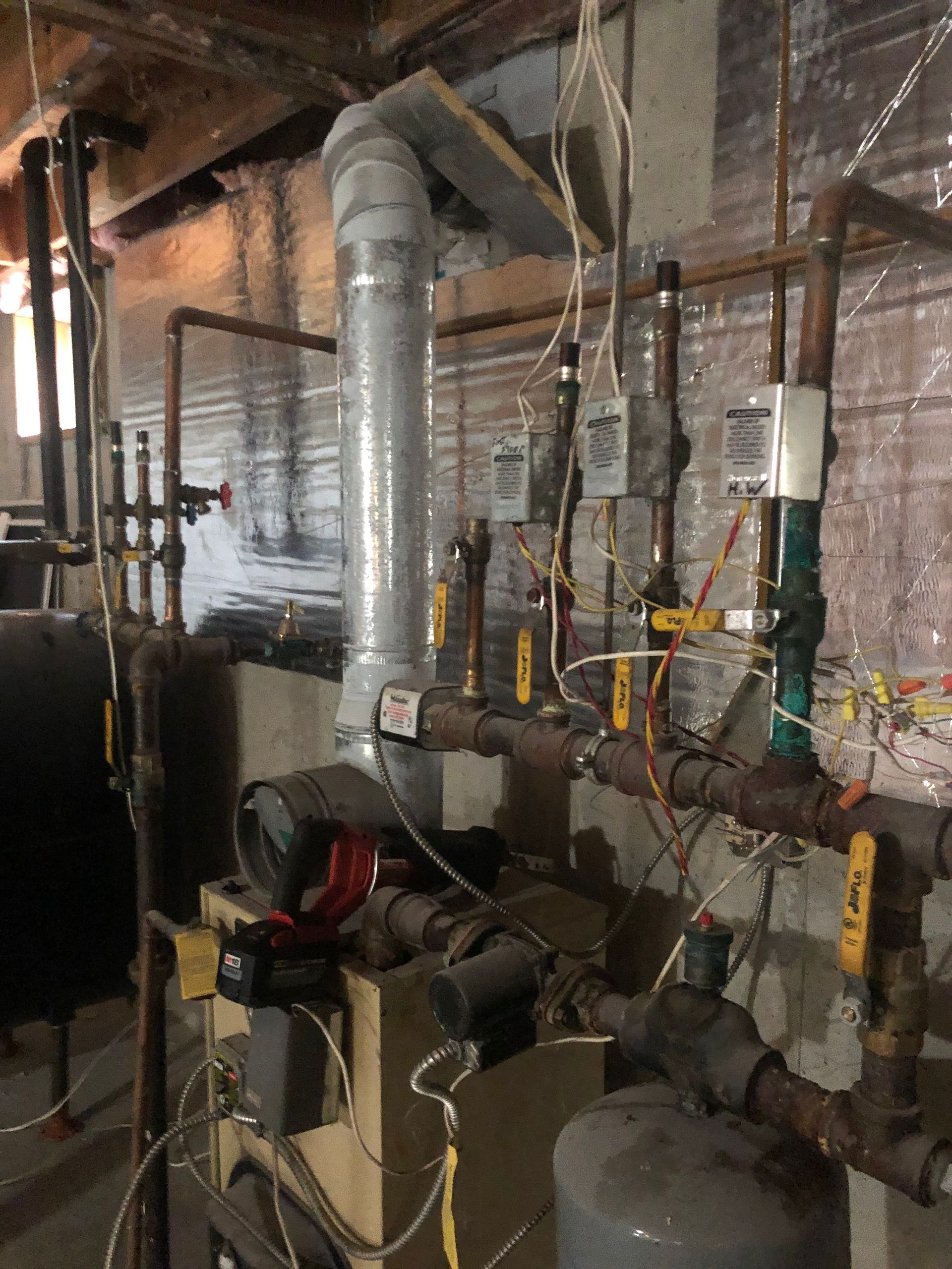 Basement utility room with pipes, water heaters, gauges, and exposed ductwork.