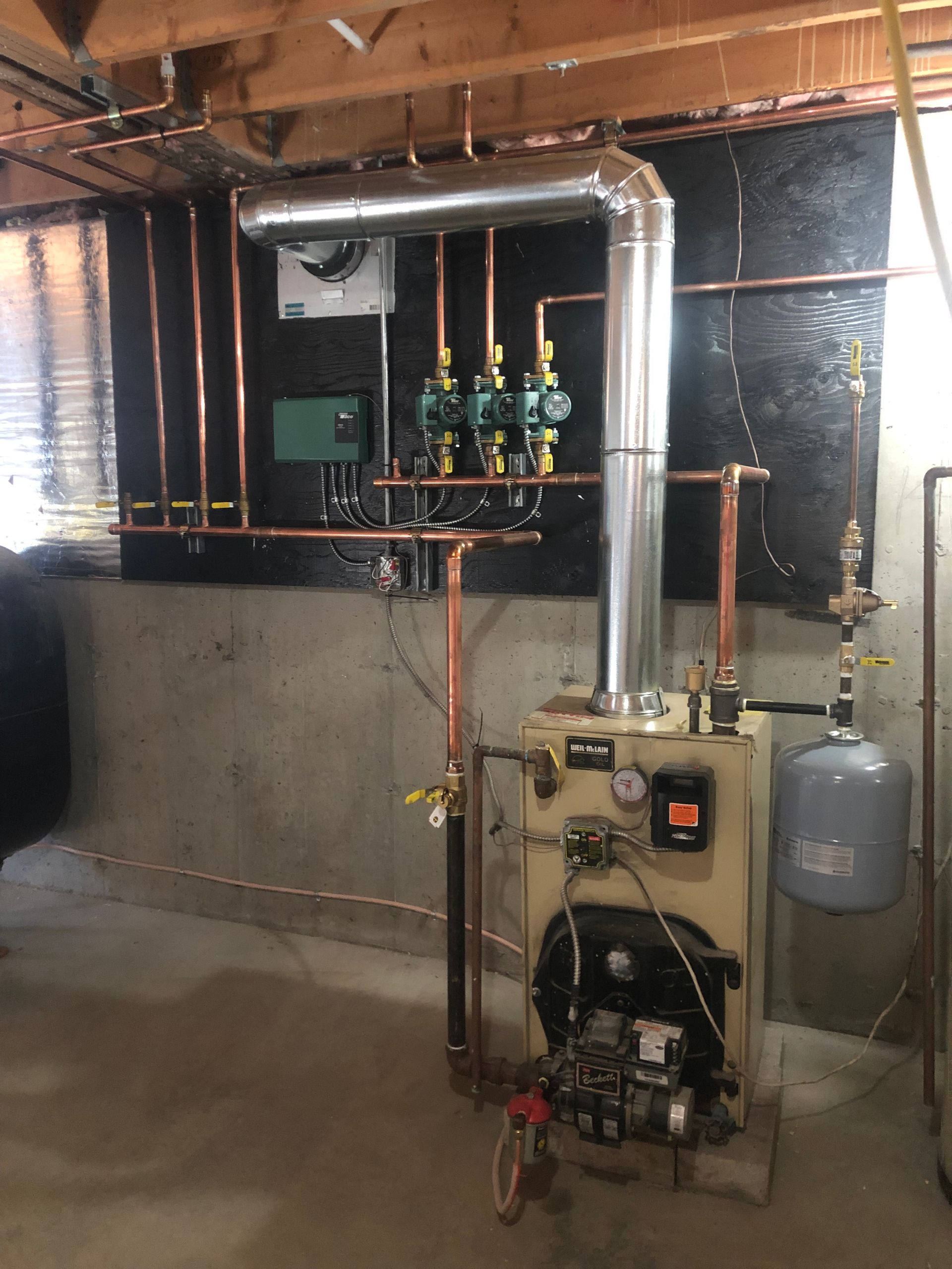 Basement boiler and water heater system with exposed pipes, valves, and a utility sink area