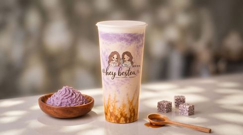 Lavender milk tea in a clear cup with purple powder, beside cubes and a spoon on a table