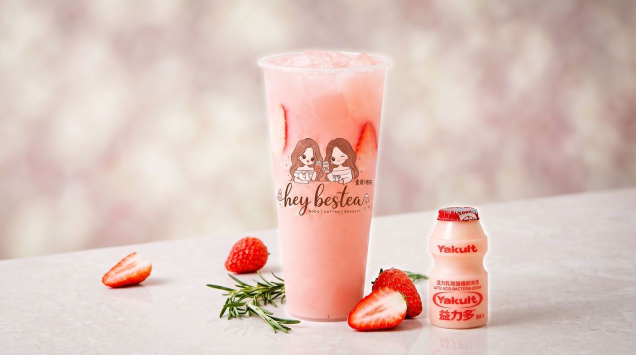 Pink iced drink with strawberries and a small strawberry yogurt bottle on a light tabletop