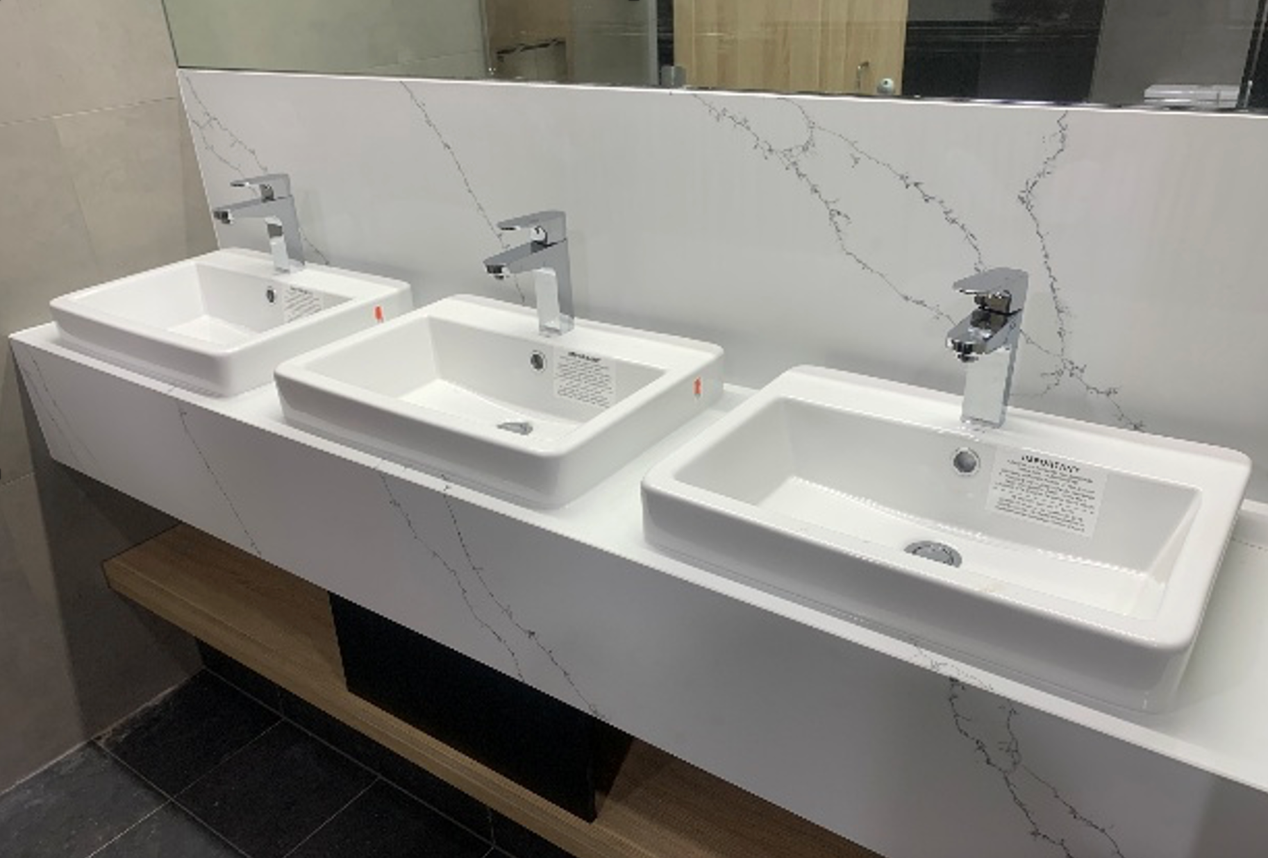 Three white sinks with silver faucets in a public restroom, set on a white countertop. — Ausplumb NT in Winnellie, NT
