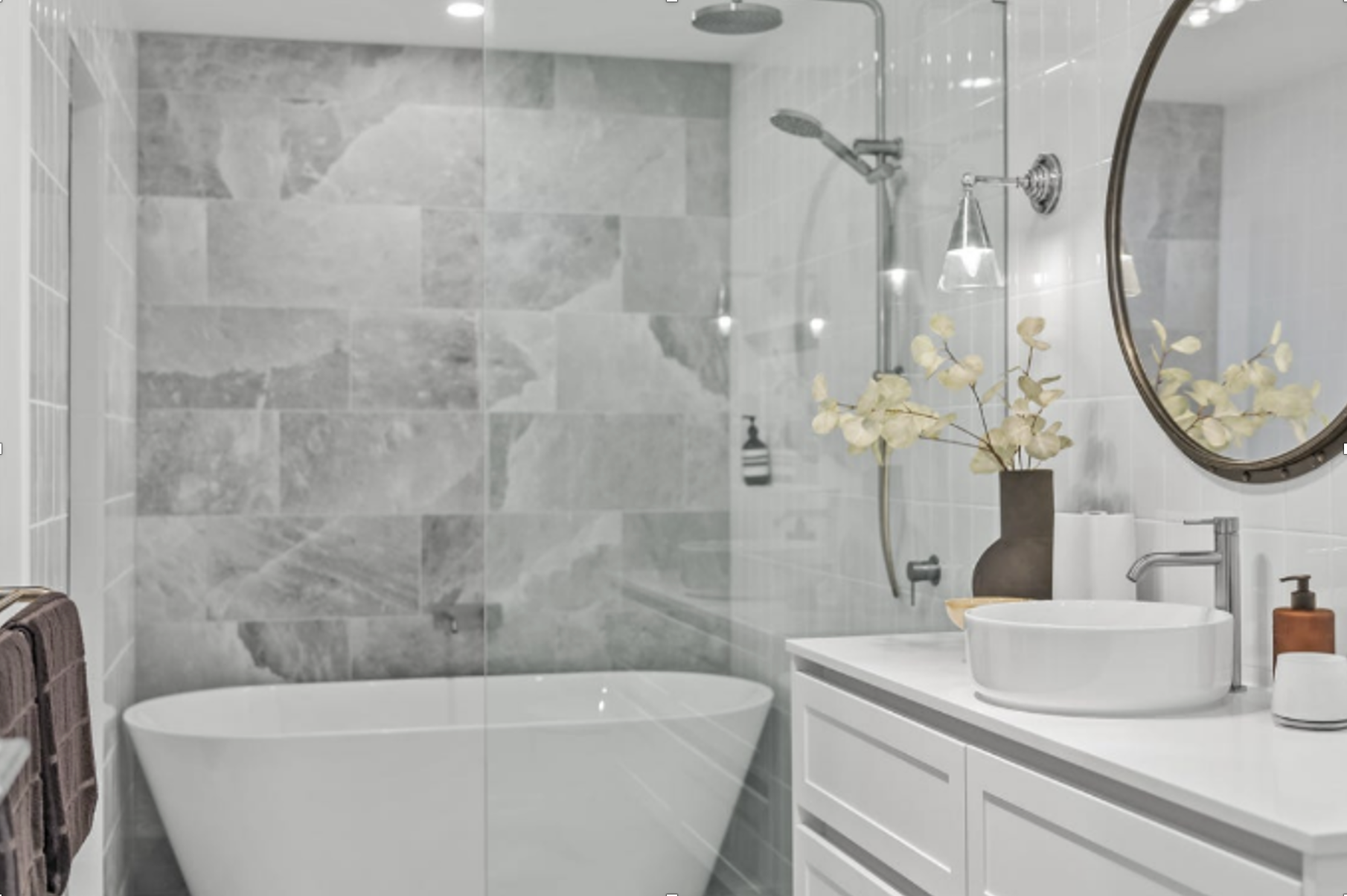 Modern bathroom with a white tub, gray tiled shower, and a white vanity with an oval mirror. — Ausplumb NT in Palmerston, NT