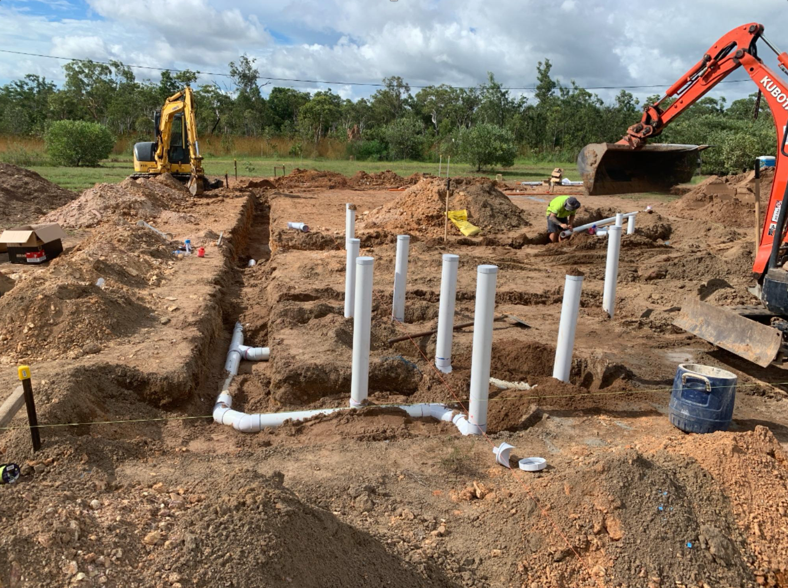 Construction site: excavator digging, workers installing white pipes in trench. — Ausplumb NT in Winnellie, NT